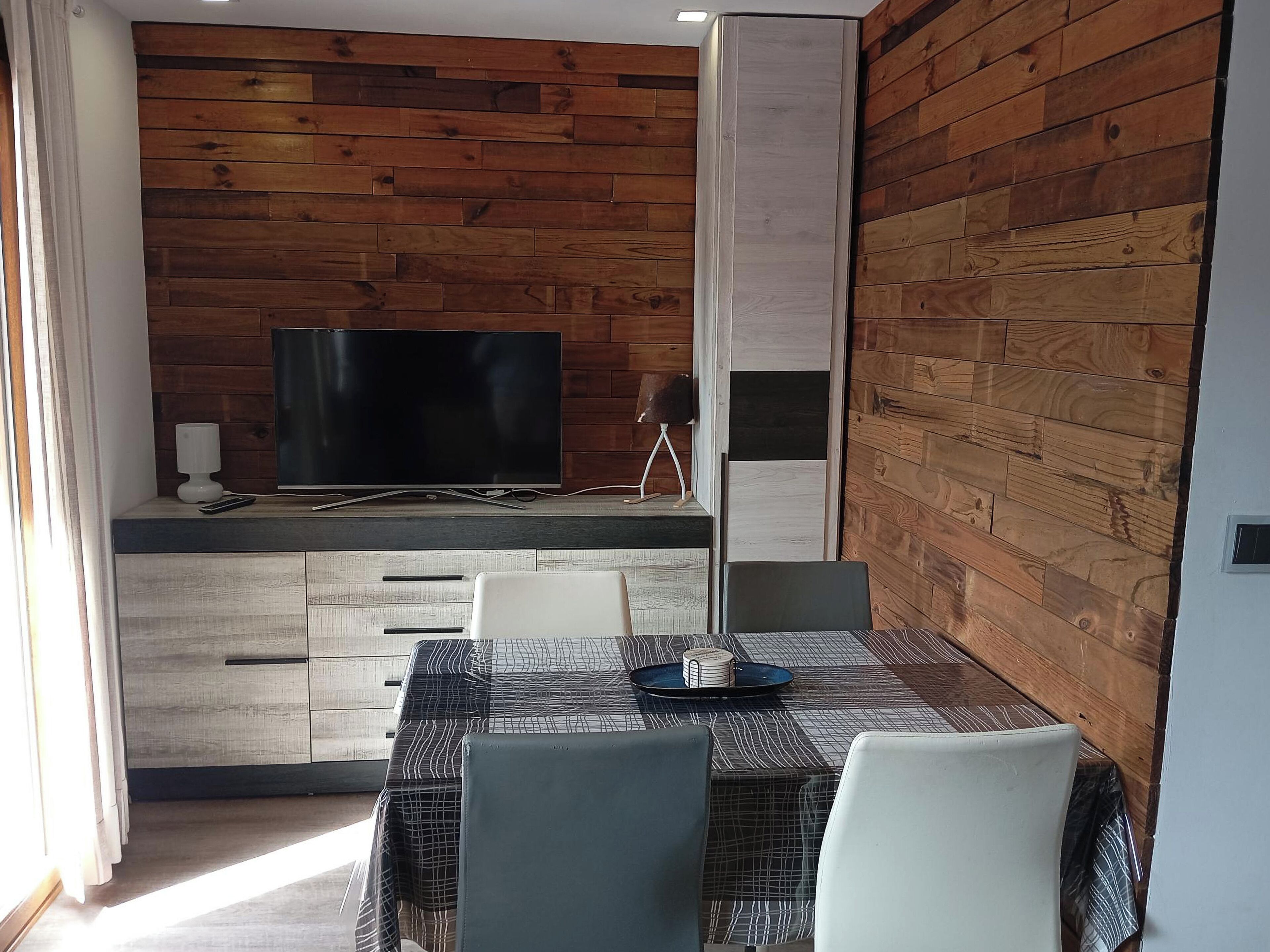 Una cocina moderna con paneles de madera, un televisor de pantalla plana y una zona de comedor con mesa y sillas.