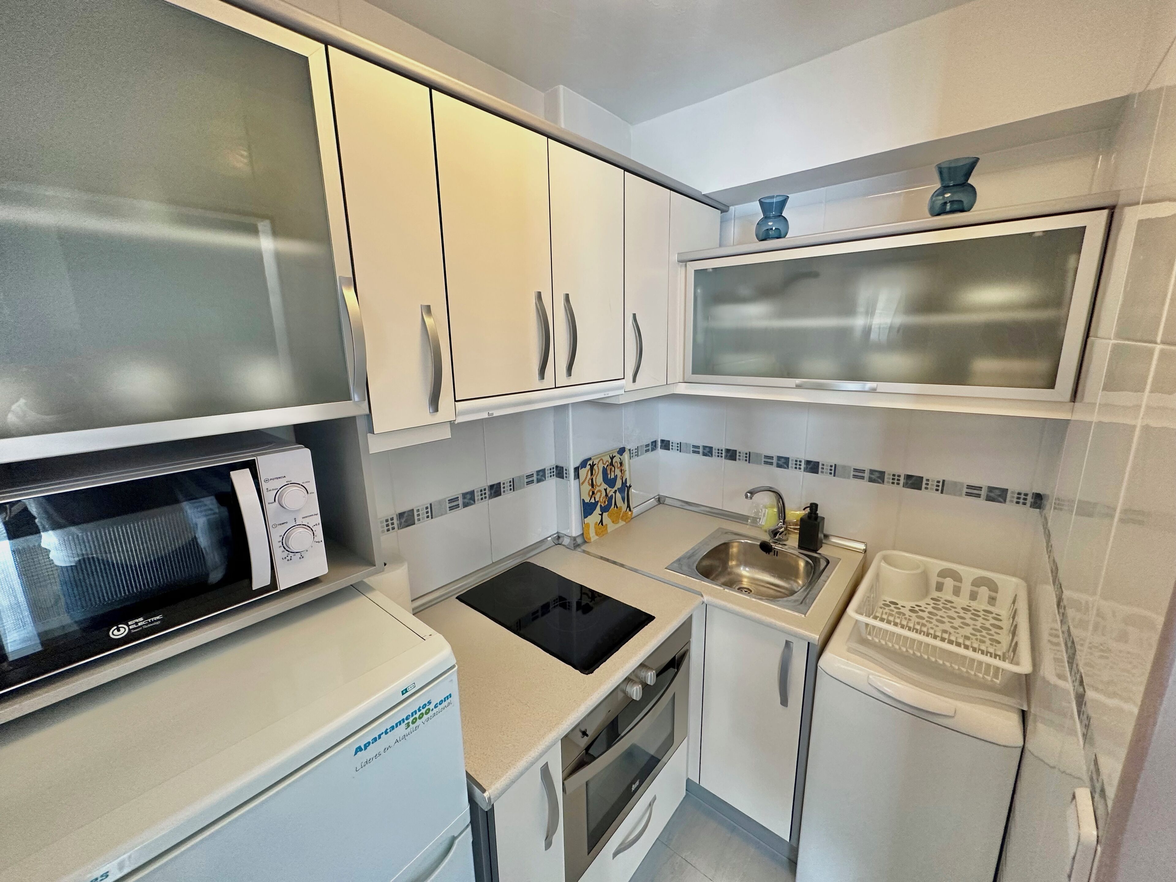 A compact kitchen with white cabinets, a microwave, a sink, and a small oven.