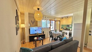 Un salon comprenant un canapé, une table à manger et un téléviseur. Il y a aussi une cuisine équipée d’un lave-linge et d’un réfrigérateur.