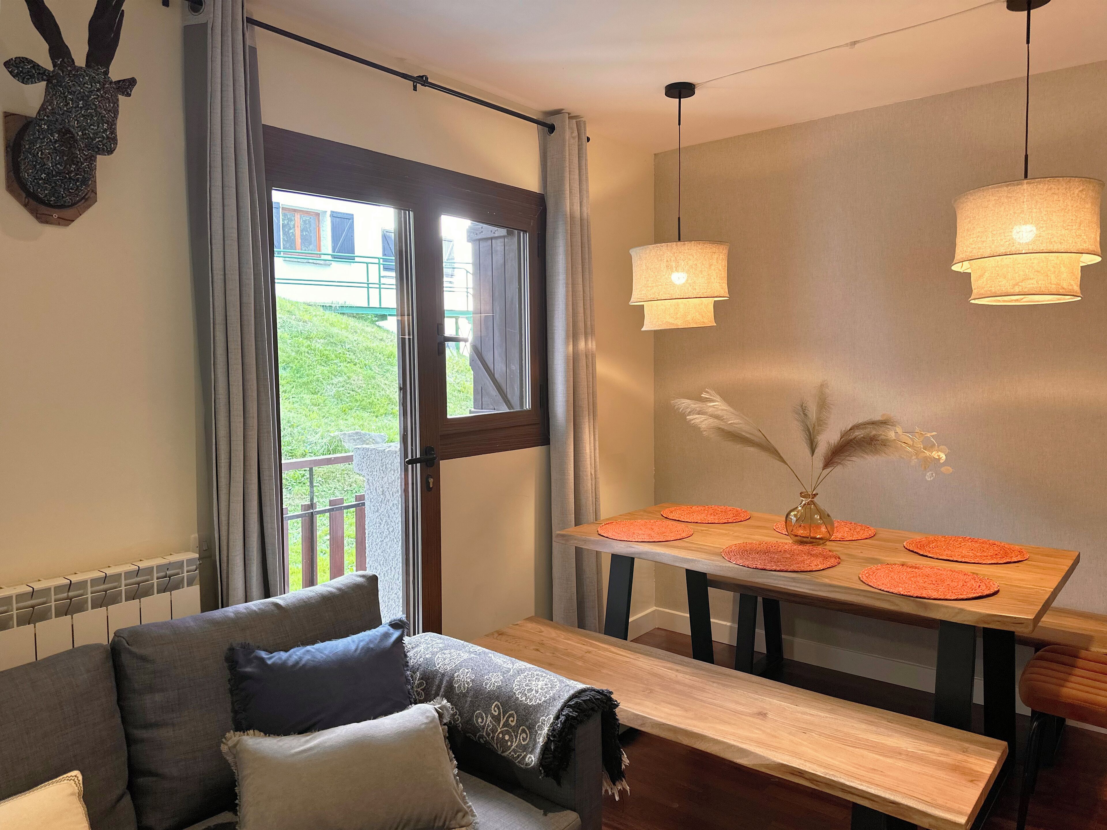 Ett mysigt rum med en soffa, ett träbord med underlägg, en dekorativ vas och ett uppstoppat djurhuvud som hänger på väggen.