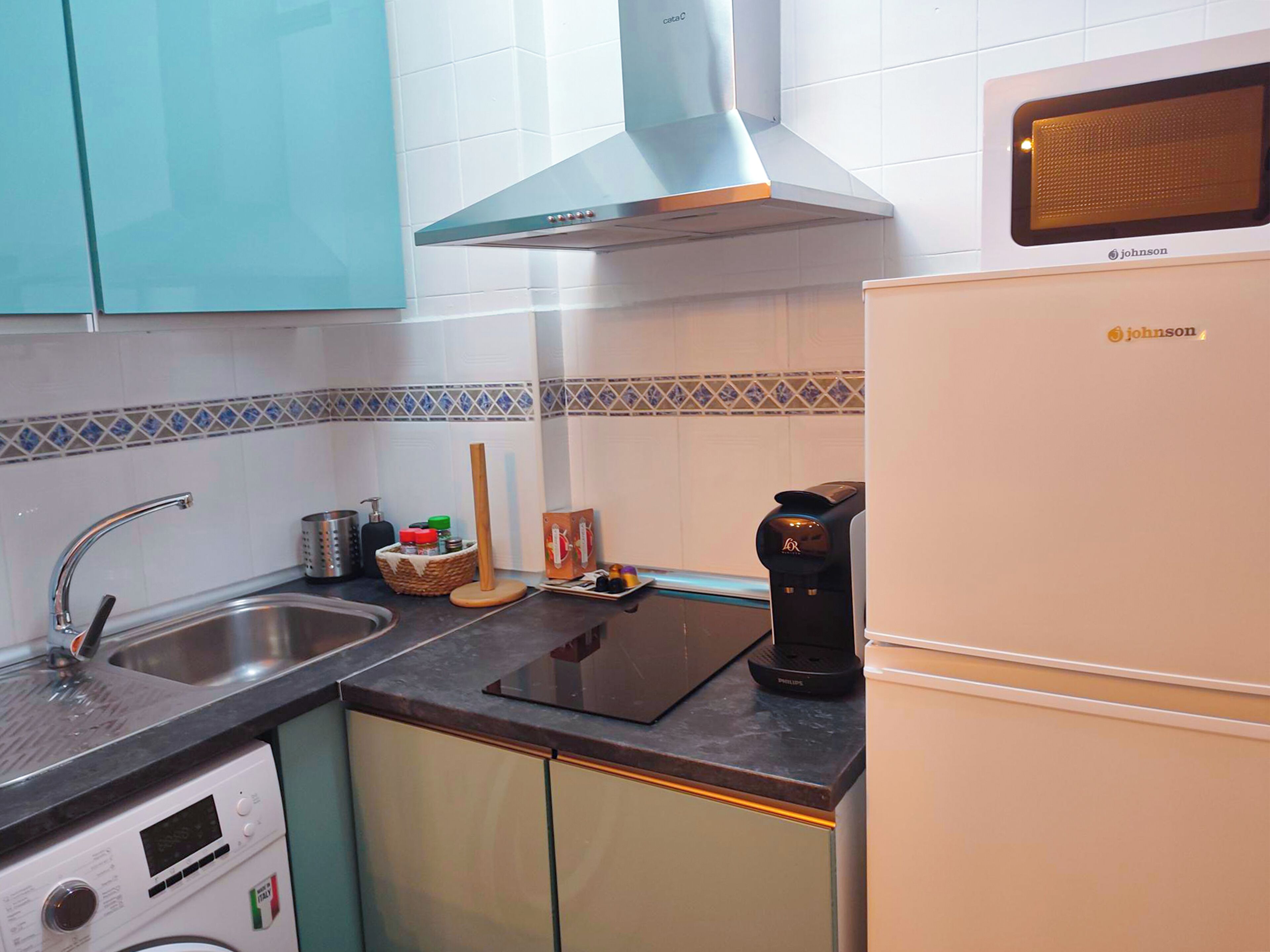 A compact kitchen with a sink, a coffee maker, a microwave, and a built-in oven.
