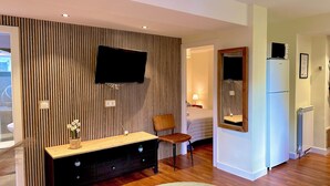 Une chambre d’hôtel moderne avec un plancher en bois, un grand miroir, un téléviseur à écran plat fixé au mur, une console en bois et un tapis rond.