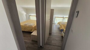 A narrow hallway leading to two bedrooms with wooden flooring and beds covered in yellow linens. - RIVIELLO ROOMS. (Marina di Camerota)