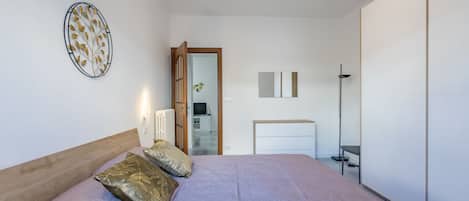 A bedroom with a bed, pillows, a bedside table, a mirror, and a wardrobe.