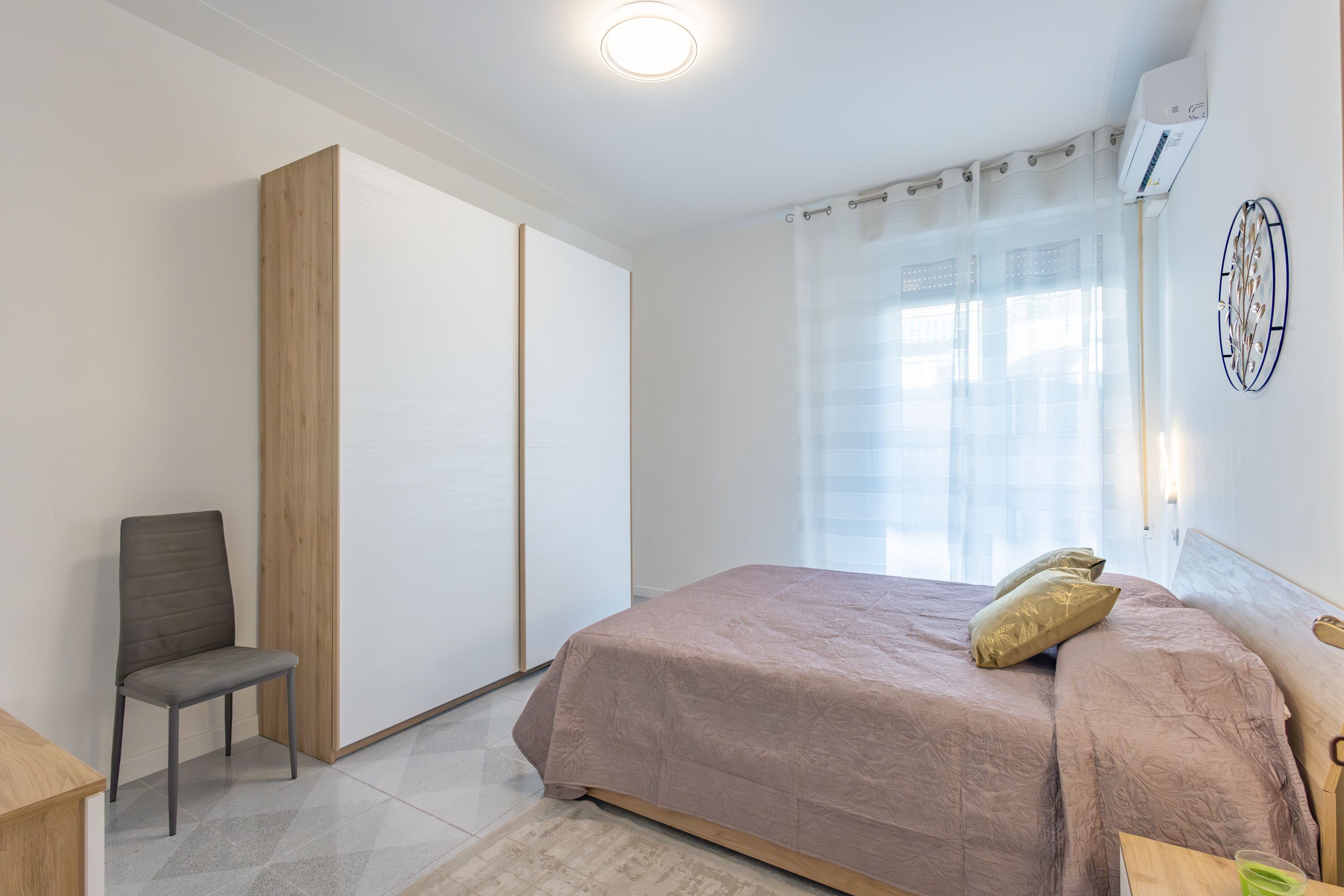 A bedroom with a bed, a chair, a wardrobe, and a window with curtains.