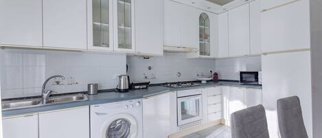 A modern kitchen with white cabinets, a washing machine, an oven, and a microwave.
