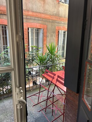 A balcony with a red metal table and chairs, a metal railing, and a view of a brick building with windows. - Le Toulousain - Hypercentre - Appartement calme en rez-de-chaussée avec Terrasse (Toulouse)