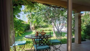 A patio with a round table and chairs, surrounded by lush greenery and trees. - La Bienvenue - Four Bedroom Villa, Sleeps 8 (Pézenas)