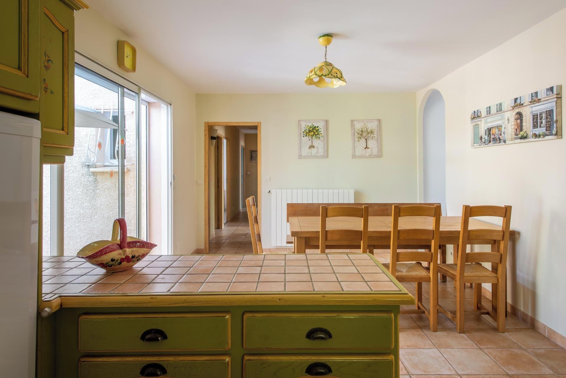 A kitchen with a green countertop, wooden chairs, a tiled floor, and a ceiling light.
