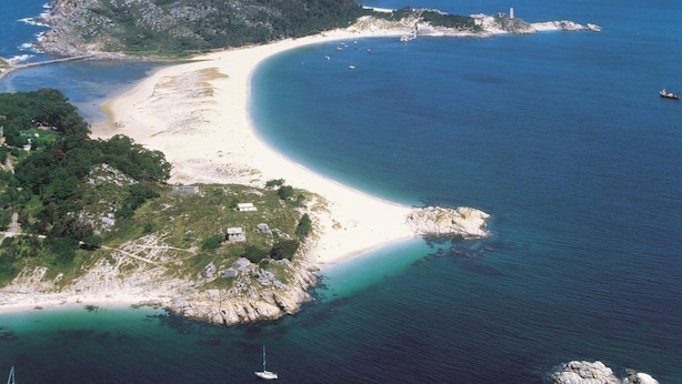 Vue aérienne d’une zone côtière avec une plage de sable, des eaux d’un bleu limpide et des affleurements rocheux.