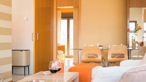 Une chambre d’hôtel avec un lit, une table à manger avec des chaises, une poubelle et un verre de vin posé sur la table.
