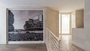 Un couloir orné d’une grande photographie encadrée représentant un paysage côtier, avec une rambarde blanche et un sol carrelé.