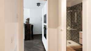 Un couloir menant à une salle de bain équipée d’une douche et dont un des murs est décoré d’un motif.