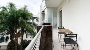 Un balcon agrémenté d’une colonne en marbre, d’une table en bois, de deux chaises noires et d’un palmier en pot.