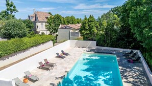 Una piscina rectangular con sillas de descanso y un muro blanco a su alrededor.