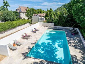 A rectangular swimming pool with lounge chairs and a white wall surrounding it.