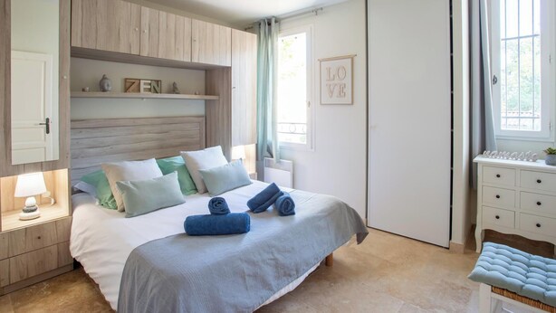 Un dormitorio con cama, mesitas de noche, armario y ventana con cortinas.