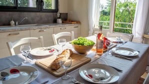 Una mesa de comedor dispuesta con platos, cubiertos, una botella de vino, hogaza de pan y un tazón de ensalada.