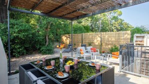 Un patio al aire libre con una mesa lista para una comida, rodeado de mobiliario de mimbre y una valla de bambú.