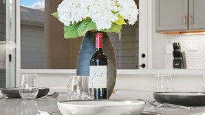 Et spisebord dækket med tallerkener, glas og bestik, en vase med hvide blomster og en vinflaske.