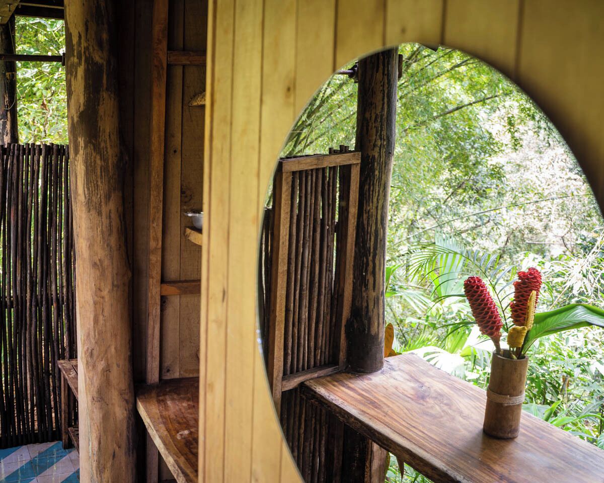 Une structure en bois comprenant un banc et une table, une porte en bois, et une vue sur la verdure à l’extérieur.