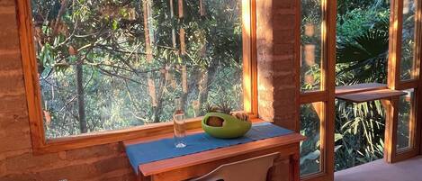 A wooden room with a table, a chair, and a large window overlooking a forest.