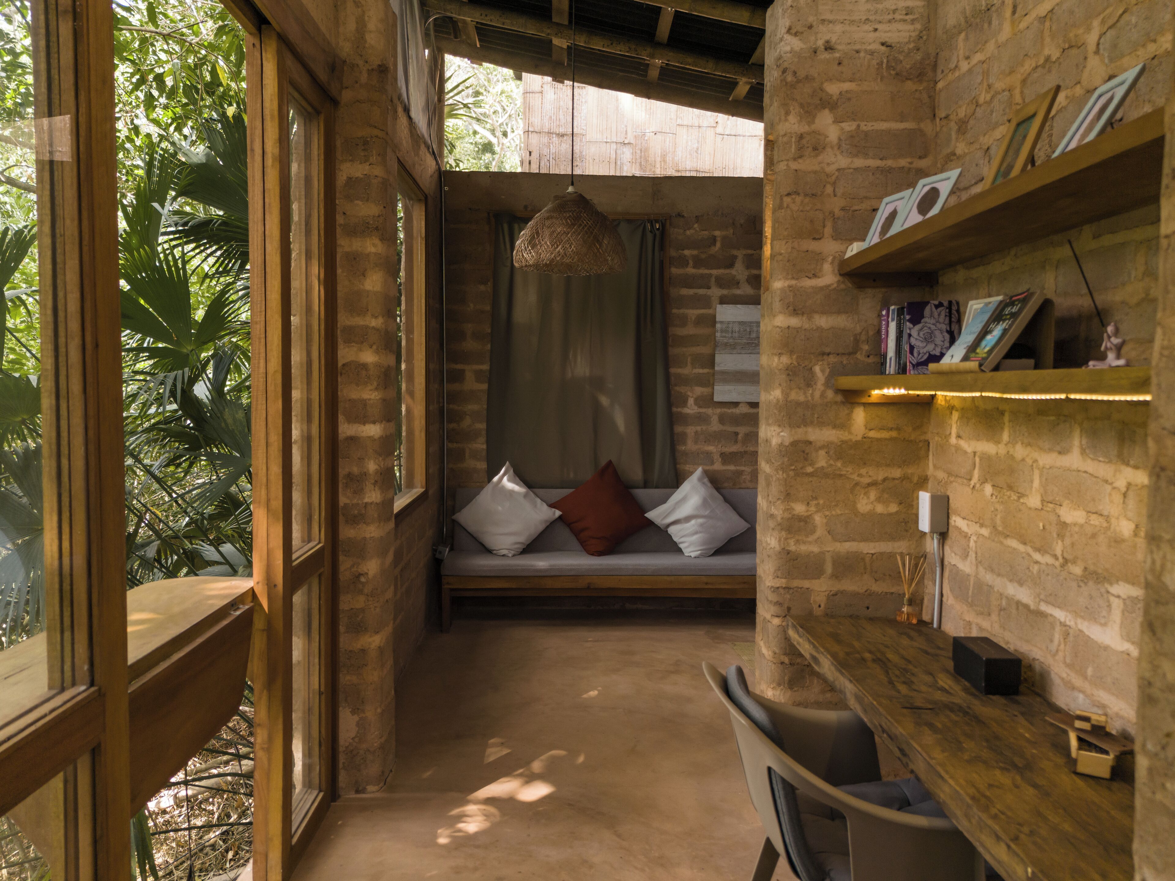 Una habitación acogedora con un banco de madera, una lámpara colgante y una pared de ladrillo con estantes.