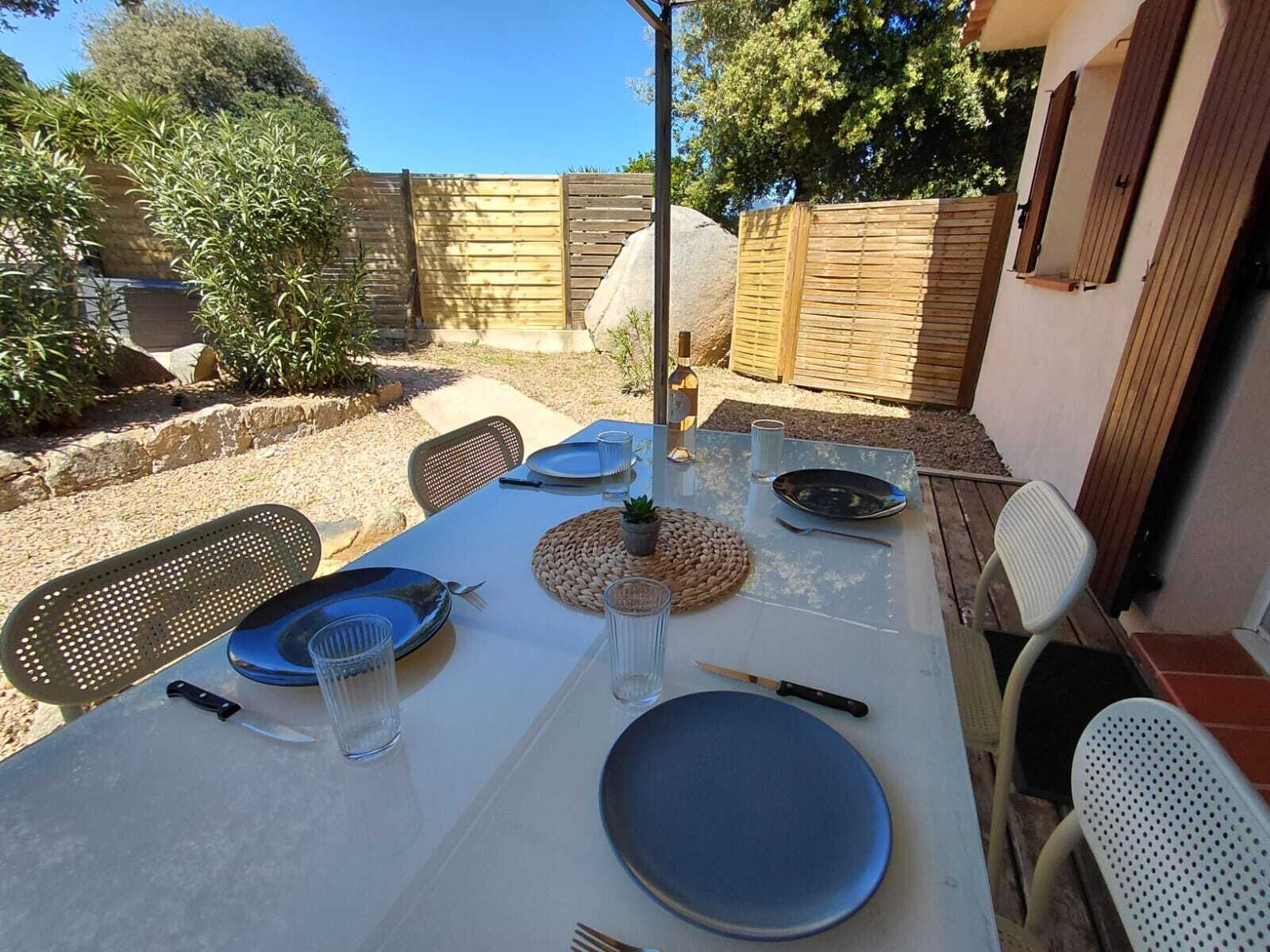 An outdoor dining area with a table set for four, surrounded by chairs, and a stone wall in the background.
