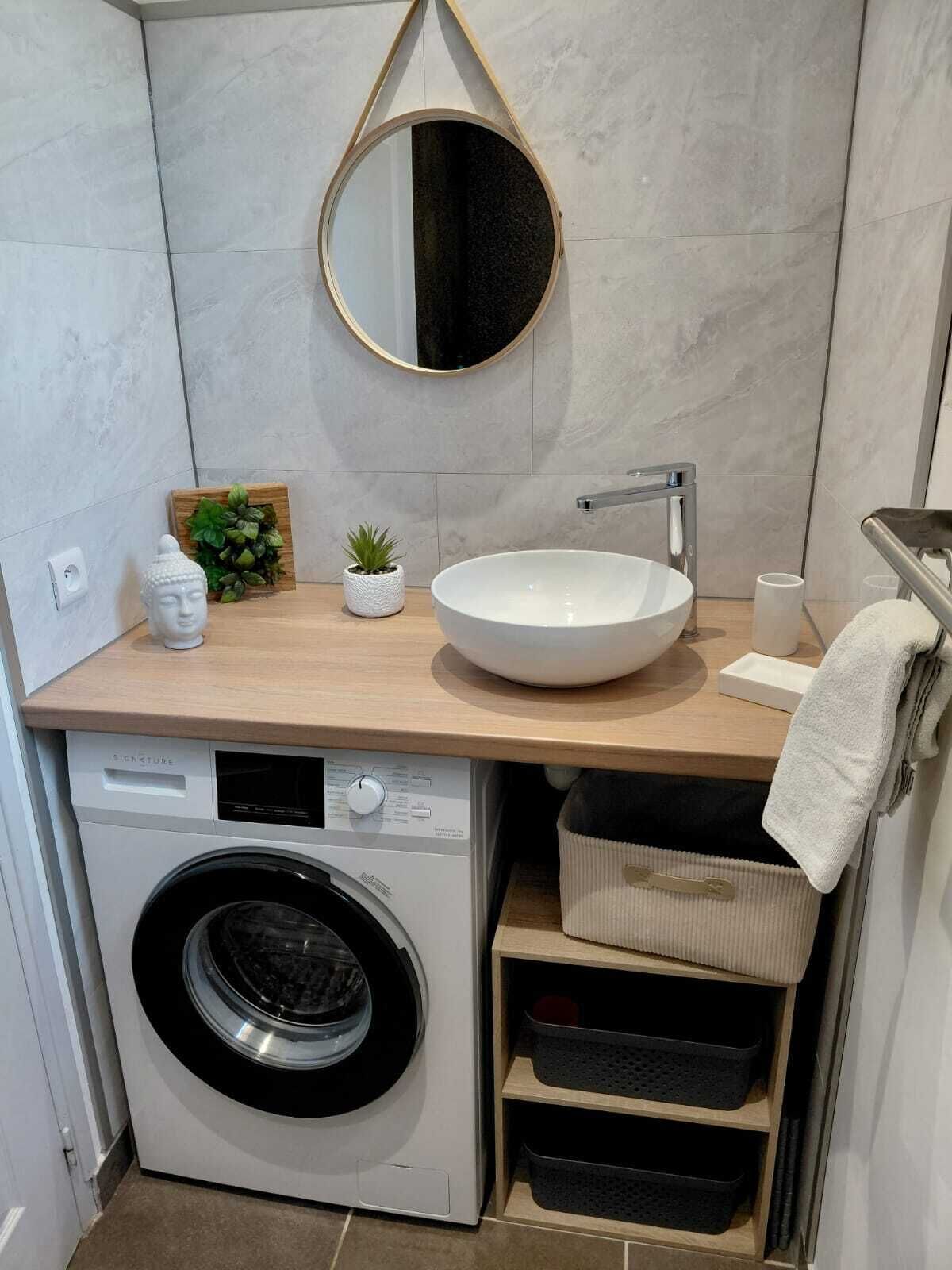 Ett litet badrum med tvättmaskin, handfat, spegel och handdukshängare.