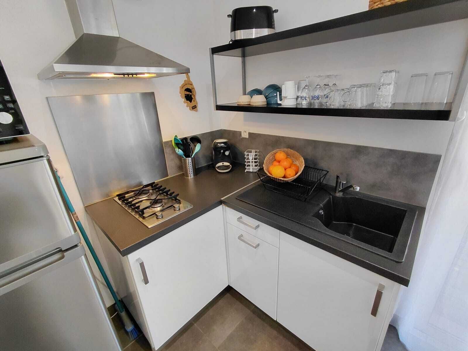 A modern kitchen with a gas stove, stainless steel range hood, white cabinets, a black countertop, a sink, and a shelf with kitchenware.