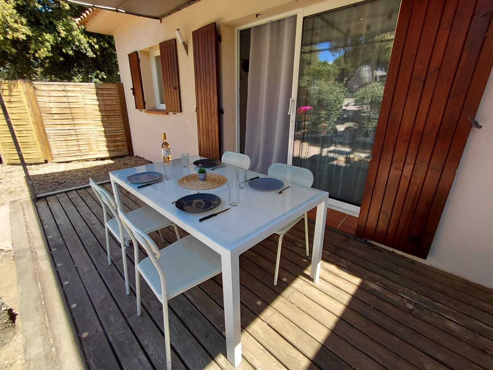 Een overdekt terras met een witte tafel voor vier personen, omringd door metalen stoelen.