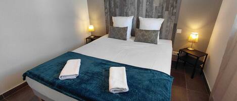 A hotel room with a bed, two bedside tables, a wall-mounted decorative piece, and a patterned headboard.