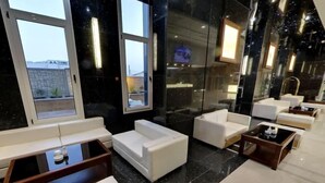 Un moderno vestíbulo de hotel con sofás blancos, una mesa de centro y un espejo grande que refleja el interior.