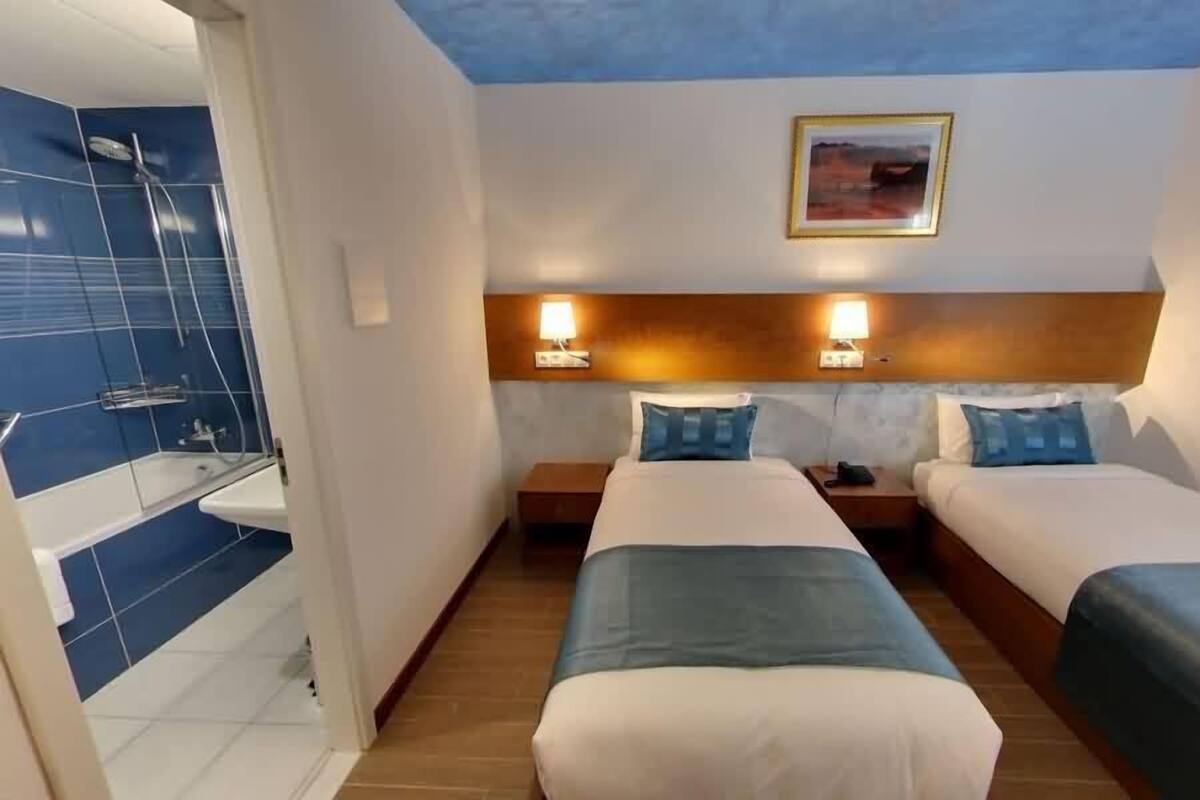 Habitación de hotel con dos camas, baño con ducha y un cuadro en la pared.