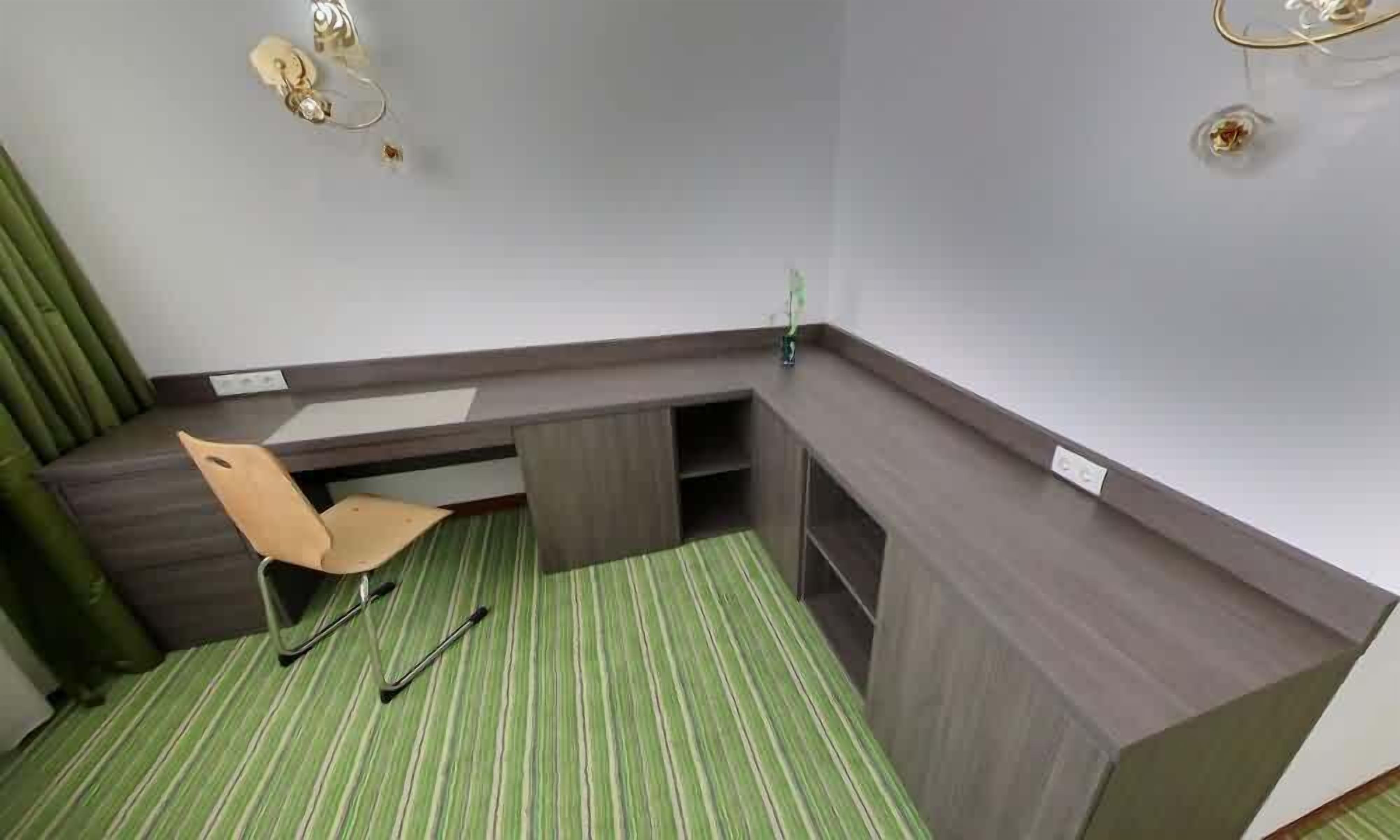 Habitación de esquina con escritorio, una silla y alfombra verde a rayas.