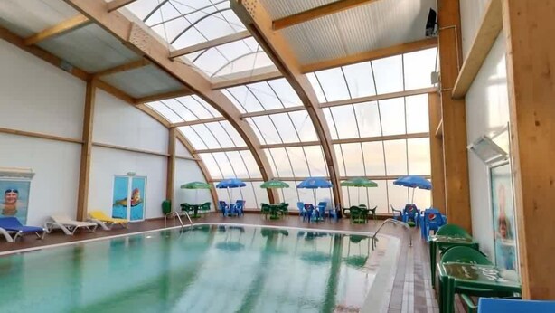 Una piscina interior con techo de cristal, sillones de descanso y sombrillas.