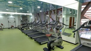 Varias bicicletas estáticas en un gimnasio con piso verde y un espejo grande en una pared.