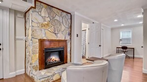 Un salon doté d’une cheminée en pierre, de fauteuils en cuir blanc et d’un parquet en bois massif.