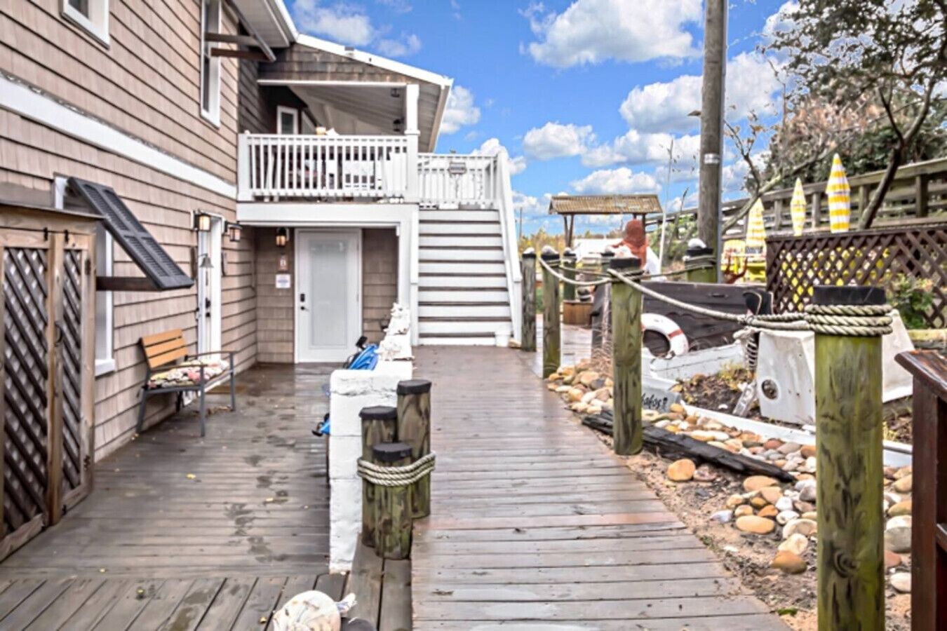 A wooden deck leading to a house with a balcony, a bench, and a small shed.