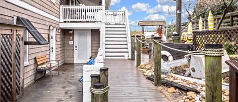 A wooden deck leading to a house with a balcony, a bench, and a small shed.