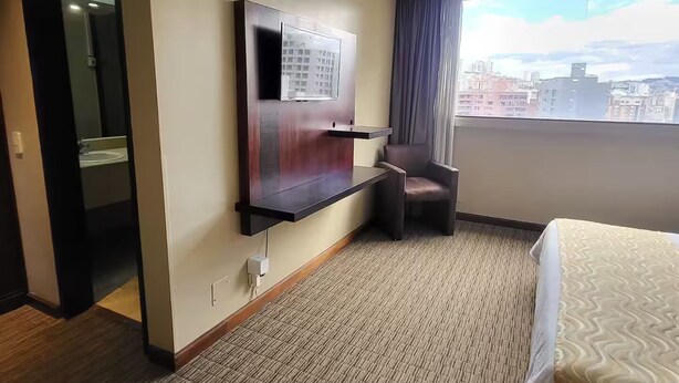 Una camera d'albergo con un letto, una sedia, una TV a parete e vista sulla città dalla finestra.