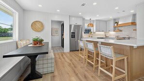 Una cocina moderna con armarios blancos, una isla central con taburetes y luces empotradas en el techo.