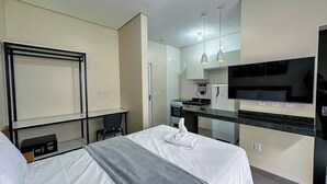 Habitación de hotel con cama, escritorio, silla, televisor, zona de cocina y baño.