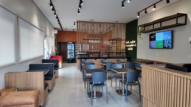 Un café moderno con muebles de madera, una zona de bar y una pantalla de televisión en la pared.