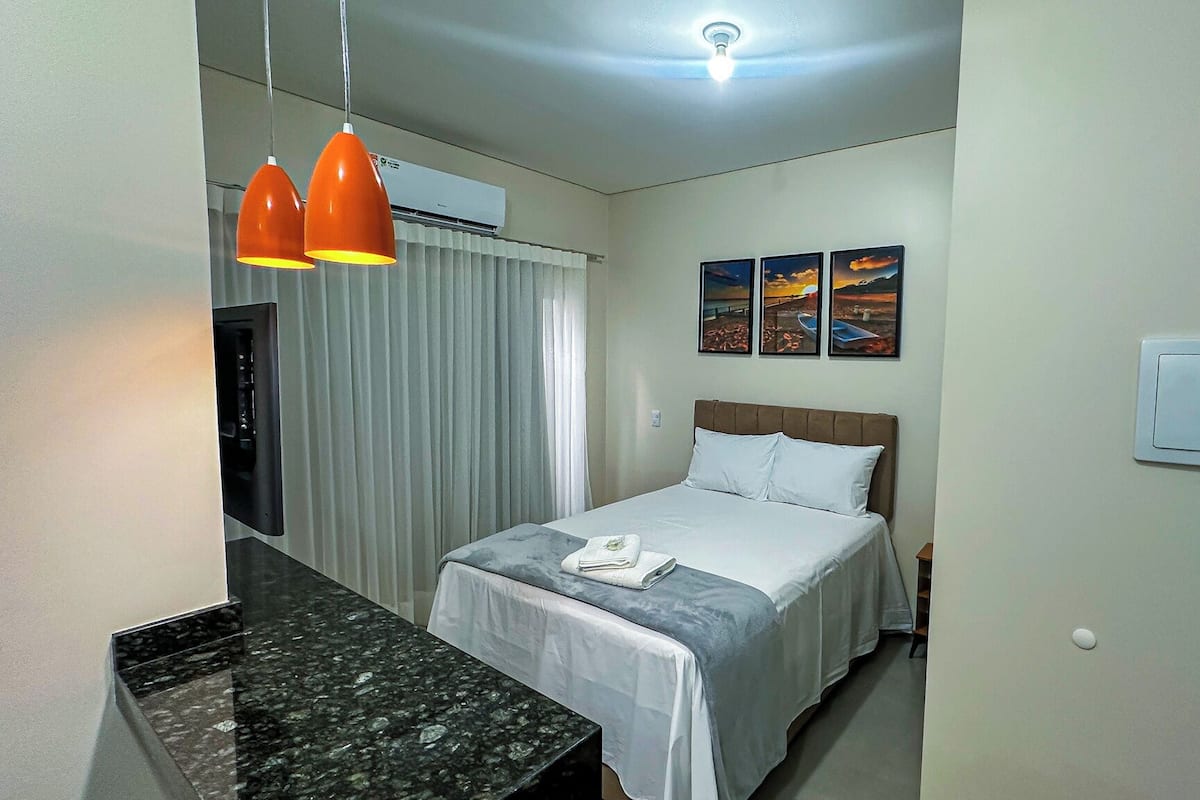 A hotel room with a bed, a desk, a mirror, and a ceiling light.