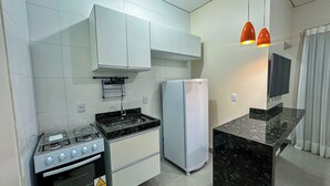 Una cocina compacta con muebles blancos, estufa a gas, refrigerador y encimera de mármol.