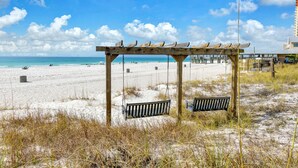 Ein Strand mit einer Holzschaukel, sandigem Ufer und einem Pier im Hintergrund.