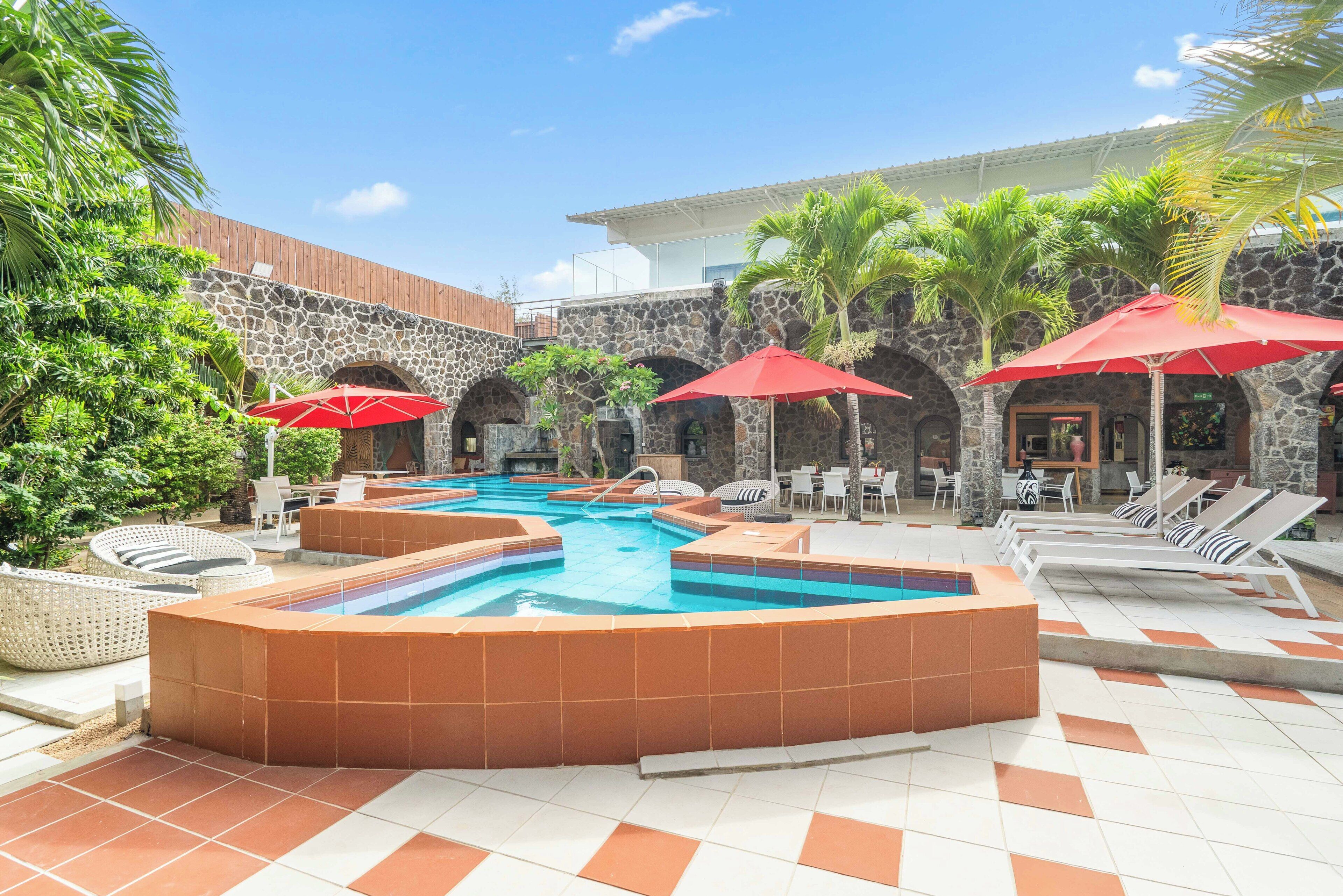 A pool area with a hot tub, lounge chairs, and umbrellas.