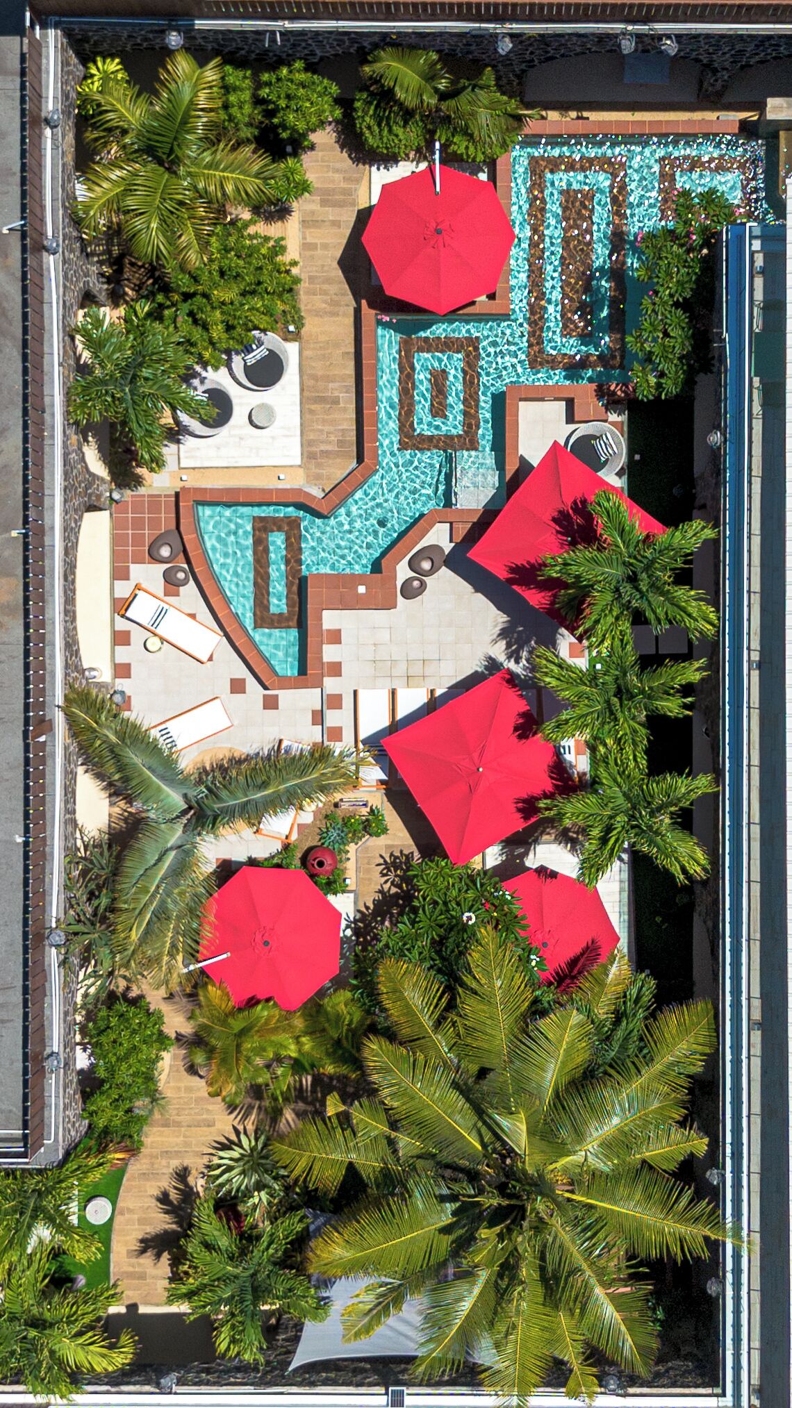 Luchtbeeld van een resort met een zwembad, palmbomen en rode parasols.