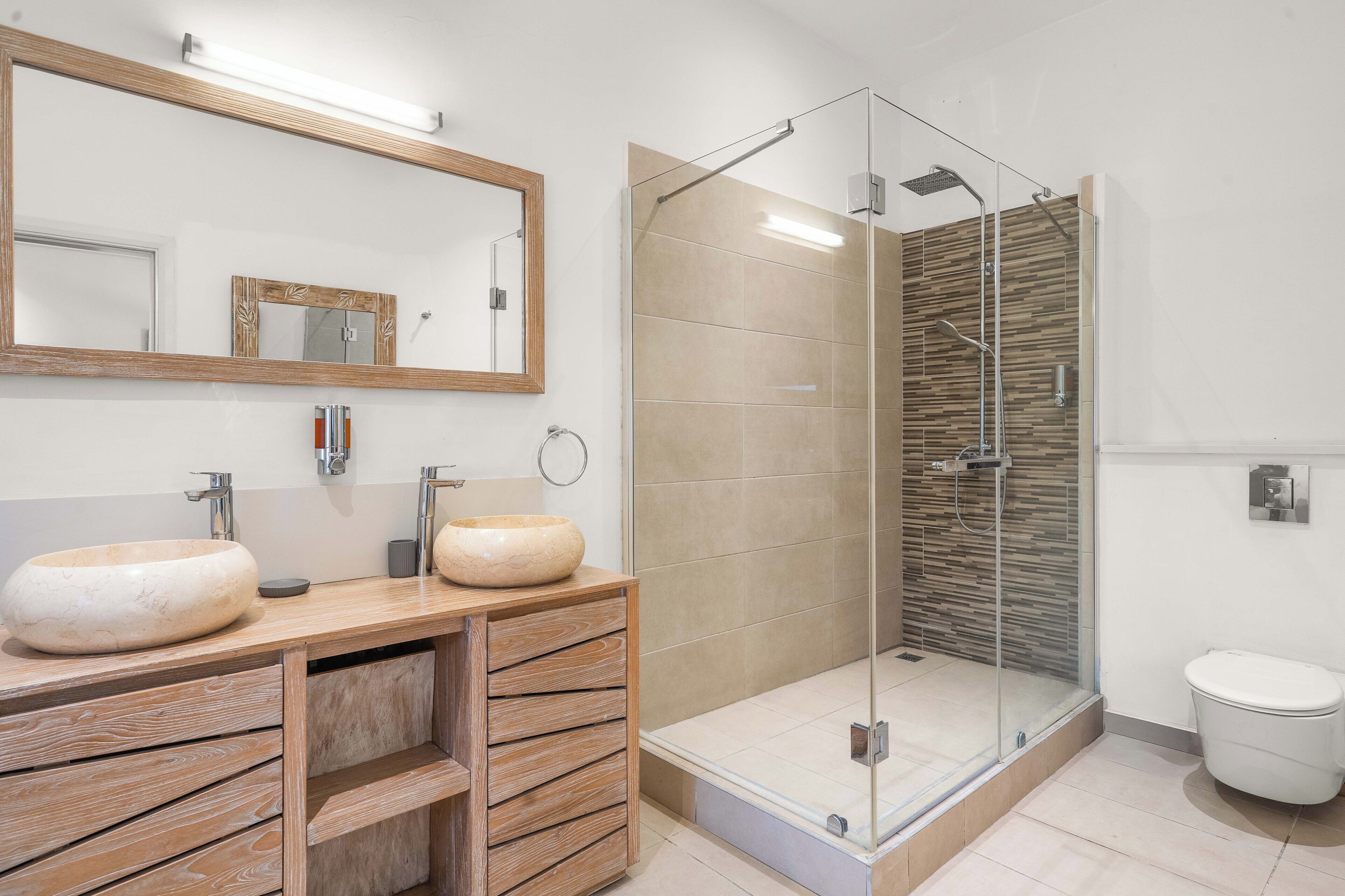 A modern bathroom with two sinks, a large mirror, a glass-enclosed shower, and a toilet.